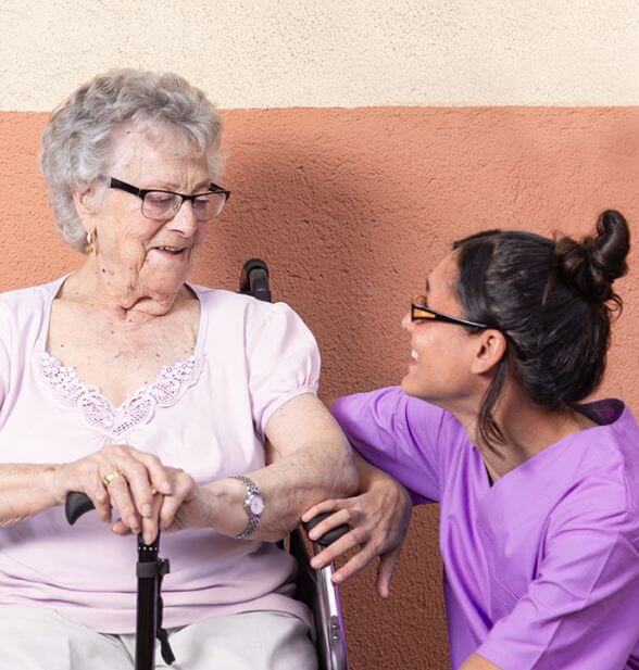 A carer chats with an elderly woman using a walker